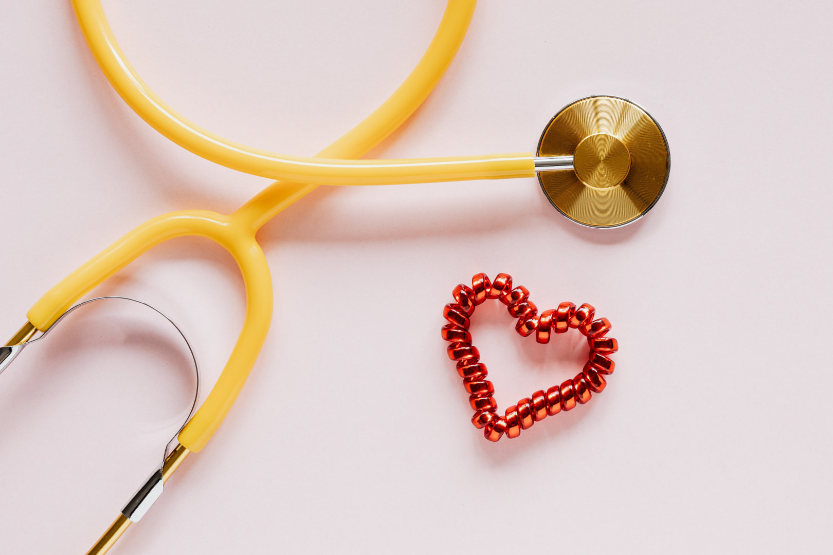 Yellow Stethoscope with a little heart made out of ribbons next to it